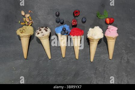 Coni assortiti di waffle fatti in casa di gelato in fila, dal sapore diverso colorato su sfondo ardesia Foto Stock