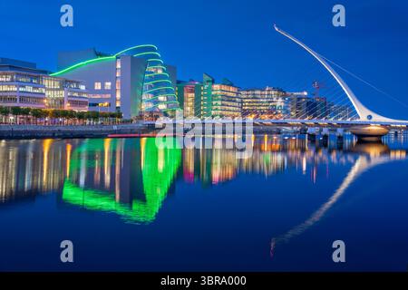 Il Centro Congressi di Dublino e il Ponte Samuel Beckett si illuminano all'ora blu, con riflessi scintillanti sul fiume Liffey e una serata blu intenso Foto Stock
