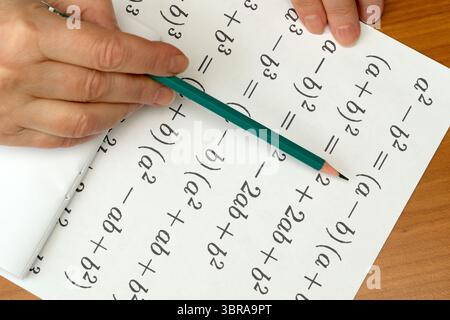 La mano di una persona scrive equazioni complesse su carta, mostrando abilità matematiche. Foto Stock