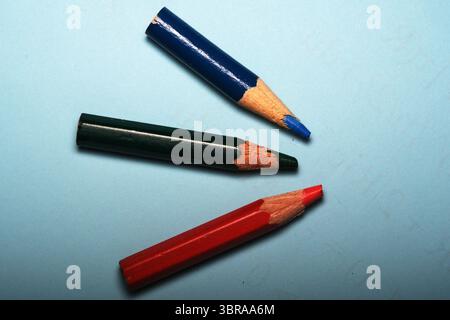 Tre matite colorate poggiano su una superficie blu rilassante, pronta per un'espressione creativa. Foto Stock