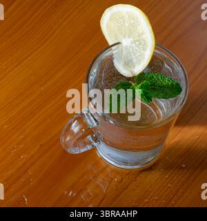 Un bicchiere di acqua frizzante con limone e menta si trova su una superficie di legno. Foto Stock