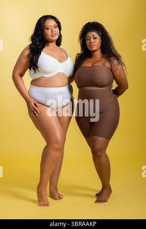 Diverse colleghe che posano su uno sfondo giallo indossando reggiseno bianco, tuta marrone e fascia Foto Stock