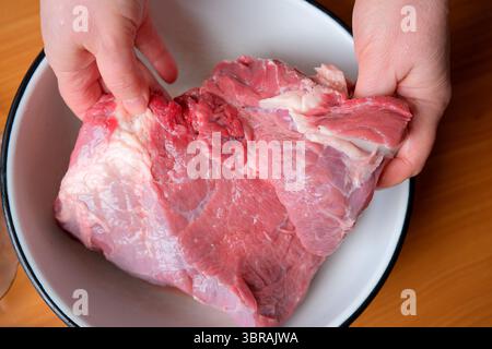 Le mani tengono un grosso pezzo di carne cruda in un recipiente, pronto per la cottura. Foto Stock