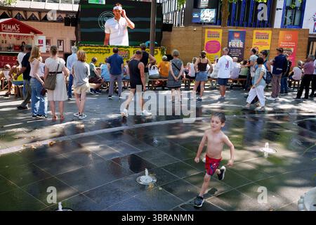 Mentre l'ondata di caldo di luglio del Regno Unito continua nel fine settimana, con gli avvertimenti di calore Met Office Amber in atto per il sud-est, il pubblico guarda la semifinale di Wimbledon tra Taylor Fritz e Carlos Alcaraz mentre i bambini spruzzano attraverso le acque rinfrescanti delle fontane di Leicester Square, l'11 luglio 2025, a Londra, Inghilterra. Foto Stock