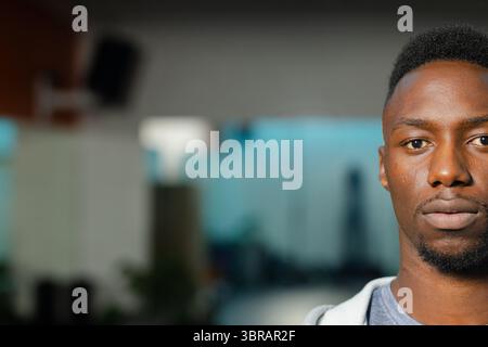 Uomo afroamericano in piedi in un ufficio open space con cappuccio vicino a altoparlante e scrivania, spazio fotocopie Foto Stock