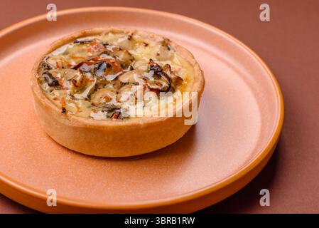 Torta o quiche, una crostata acida con pollo e funghi, spezie ed erbe aromatiche su sfondo di cemento scuro. Quiche rotonde con pollo Foto Stock