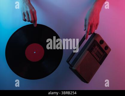 Onda retrò 80S.. Mani con ricevitore radio e registrazione in vinile. Pop art creativa di colore rosa blu neon. Illuminazione gradiente di tendenza. Luce notturna Foto Stock