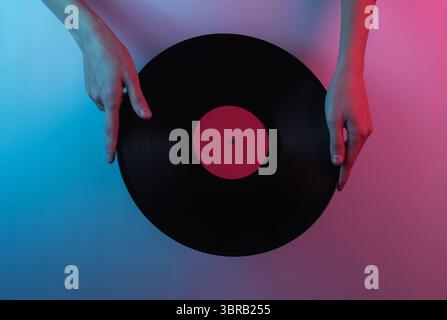 Onda retrò 80S.. Mani che tengono un disco in vinile. Pop art creativa di colore rosa blu neon. Illuminazione gradiente di tendenza. Luce notturna Foto Stock