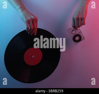 Onda retrò 80S.. Mani che tengono in mano dischi in vinile e audiocassette. Pop art creativa di colore rosa blu neon. Illuminazione gradiente di tendenza. Luce notturna Foto Stock