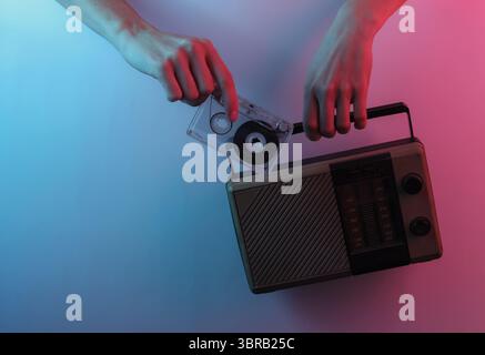 Onda retrò 80S.. Mani con ricevitore radio e audiocassetta. Pop art creativa di colore rosa blu neon. Illuminazione gradiente di tendenza. Luce notturna Foto Stock