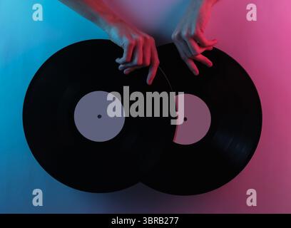 Onda retrò 80S.. Mani con dischi in vinile. Pop art creativa di colore rosa blu neon. Illuminazione gradiente di tendenza. Luce notturna Foto Stock