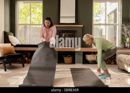 Diverse amiche composte che stendono tappeti neri nel soggiorno accanto al caminetto a legna Foto Stock