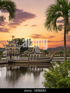 Vista al tramonto della chiatta reale Mahligai ornata su un lago presso la Moschea Sultan Omar Ali Saifuddien, Bandar seri Begawan, Brunei, incorniciata da palme Foto Stock