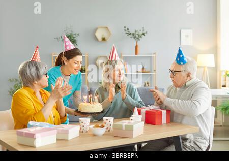 Buon anziano che festeggia il compleanno con dolci e regali, godendo momenti festivi con la giovane infermiera. Foto Stock