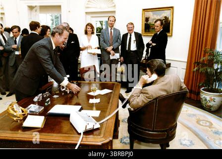 Washington, Stati Uniti d'America. 22 novembre 2009. Il capo di stato maggiore della Casa Bianca James A. Baker, III, offre un bicchiere di champagne al presidente degli Stati Uniti Ronald Reagan mentre parla con il presidente della camera Thomas P. "Tip" o'Neill al telefono nell'ufficio ovale della Casa Bianca mercoledì 29 luglio 1981. I membri dello staff Karna Small, David Gergen, Edwin Meese e il vicepresidente George H.W. Bush guardano su.credito obbligatorio: Michael Evans - Casa Bianca tramite CNP/Sipa USA Credit: SIPA USA/Alamy Live News Foto Stock