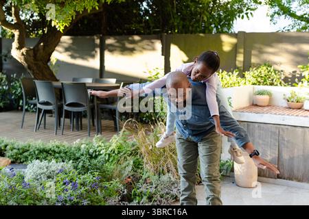 Padre afroamericano che porta la figlia sul patio in pietra del cortile con tavolo da pranzo Foto Stock