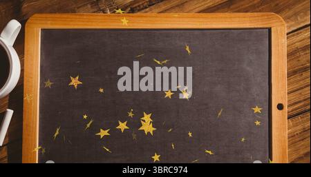 Con lavagna incorniciata distesa sul tavolo, coriandoli con stelle dorate, tazza da caffè e gesso Foto Stock