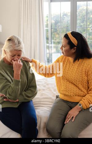 Diverse amiche si siedono sul letto in camera da letto con una coperta a motivi geometrici, confortante anziano turbato Foto Stock