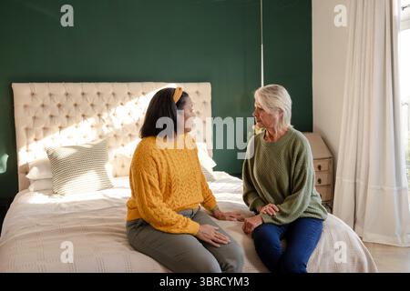 Diverse amiche si siedono sul bordo del letto in camera da letto con testiera in tufo e cuscino di lancio Foto Stock