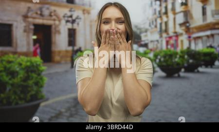 Donna sorridente e baciata alla macchina fotografica in una vivace scena di strada cittadina caratterizzata da architettura classica e vegetazione lussureggiante. Foto Stock