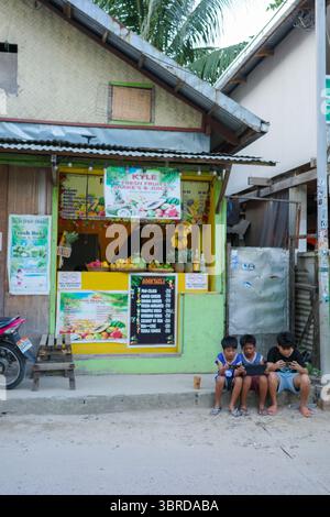 Un gruppo di tipi che giocano insieme di fronte a un negozio di Street food locale, vendendo frutta fresca e frullati a Palawan, Filippine Foto Stock