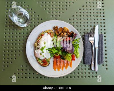 Piatto da buongustai con uova in camicia, pane tostato all'avocado, salmone affumicato e insalata fresca. Vista dall'alto. Brunch sano ed equilibrato con toast all'avocado Foto Stock