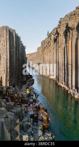 I visitatori si meravigliano davanti alle impressionanti colonne di basalto del canyon Studlagil, annidato nella natura selvaggia e panoramica delle Icelands. Le acque cristalline scorrono tra le torreggianti scogliere, creando una meraviglia naturale mozzafiato. Foto Stock
