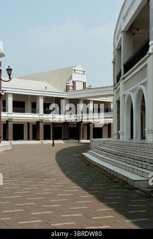 Una piazza vuota e deserta con un moderno edificio di architettura classica. Archi e colonne in una luminosa giornata di sole, con pavimentazione in mattoni a motivi geometrici e shado Foto Stock