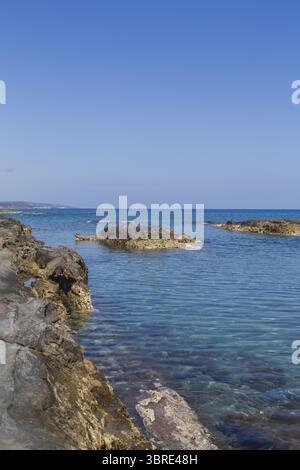 Vista della costa rocciosa che incontra il mare turchese sotto un cielo azzurro, con texture baciate dal sole e coste lontane, Dipkarpaz, Cipro del Nord, Cipro. Foto Stock