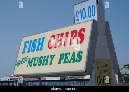 Fish Chips con cartello Mushy Peas sul lungomare e sulla spiaggia di Brighton nell'East Sussex, Inghilterra. Molo sullo sfondo. Foto Stock