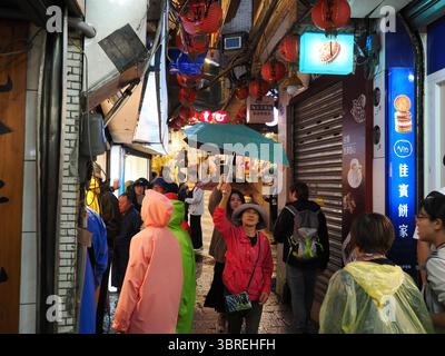 Jiufen, Taiwan - 8 novembre 2024 - i turisti con ombrelloni e impermeabili esplorano un vivace vicolo decorato con lanterne nella vecchia via di Jiufen su una pioggia Foto Stock