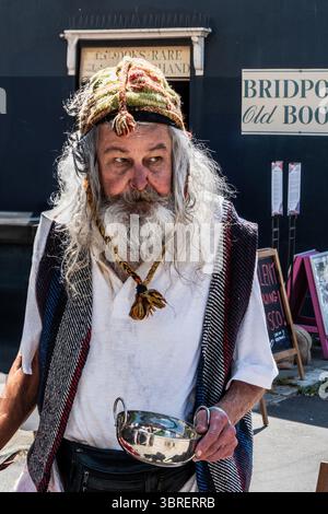 Personaggio eccentrico in stile boemo con una ciotola argentata che attraversa Bridport, Dorset. Stile di vita hippy, creativo, artistico, colorato. Foto Stock