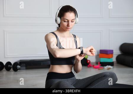 Donna che controlla il fitness tracker durante l'allenamento in casa Foto Stock
