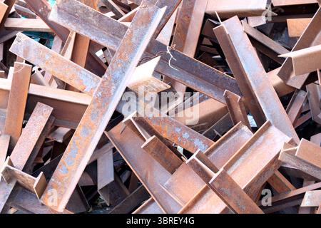Impilate in alto in un cantiere di rottami, travi in acciaio intemperie si intrecciano in una gamma vivace. Foto Stock