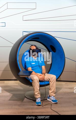 Uomo seduto con un visore VR (realtà virtuale) al salone dell'automobile, prova la demo virtuale Mercedes EQ. Salone dell'automobile IAA Foto Stock