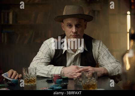 Uomo vestito d'epoca a un tavolo fumé poco illuminato mentre giocava a poker Foto Stock