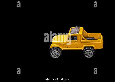 Modello in miniatura giallo di un pick-up 4x4 su sfondo nero, posizionato a destra con spazio vuoto a sinistra per il testo o il marchio. Formato orizzontale. Foto Stock