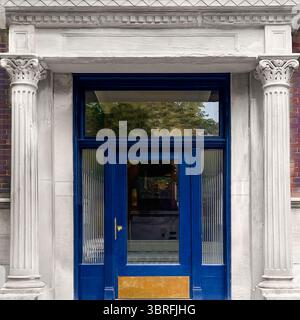 Porta blu navy con accenti dorati incastonata tra colonne in pietra classica e capitelli ornati, un ingresso neoclassico in un edificio residenziale di Chicago. Foto Stock