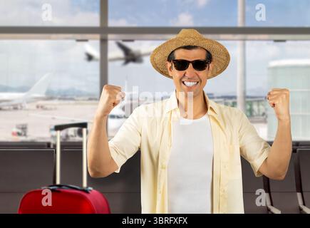 Uomo in vacanza che indossa una maglietta gialla, cappello estivo, occhiali da sole all'aeroporto. Molto felice ed eccitato facendo un gesto vincente con le braccia alzate, sorridenti e urla Foto Stock
