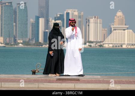 Una coppia si trova accanto all'acqua, godendosi il sole. Un uomo e una donna in abiti arabi tradizionali camminano lungo l'argine contro il dorso Foto Stock