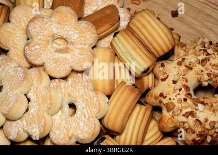 Deliziosi biscotti assortiti sono preparati ad arte su un piatto rustico di legno, invitando gli ospiti a viziarsi. Le texture e le forme vivaci creano un ambiente caldo Foto Stock