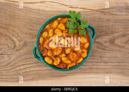 Fagioli di burro stufati con salsa di pomodoro e salsicce di maiale a fette, su un tavolo in legno di quercia Foto Stock