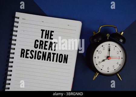 Il testo delle grandi dimissioni scritto sul blocco note con sveglia su sfondo blu Foto Stock