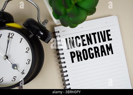 Testo del programma di incentivazione scritto sul blocco note con sveglia Foto Stock