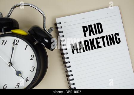 Testo marketing a pagamento scritto su blocco note con sveglia Foto Stock