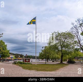 Sodertalje, Svezia - 6 giugno 2025: Una vista panoramica di un parco sul lungomare con una bandiera svedese su un palo alto, circondato da vegetazione lussureggiante e alberi. Foto Stock