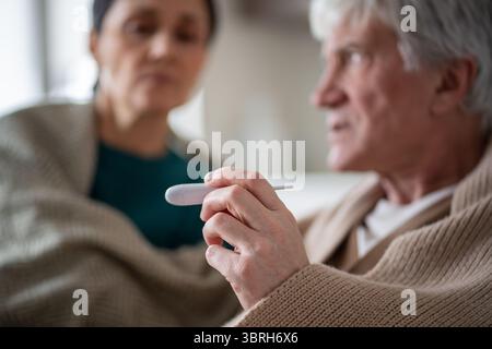 Monitoraggio della temperatura durante la malattia. Coppia di anziani sotto copertura per malattia, malattia condivisa Foto Stock