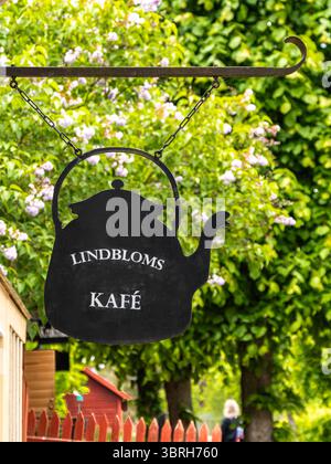 Sodertalje, Svezia - 6 giugno 2025: Un segno nero di una teiera appesa a una staffa metallica, che pubblicizza "Lindbloms Kafé". L'impresa di fondo Foto Stock