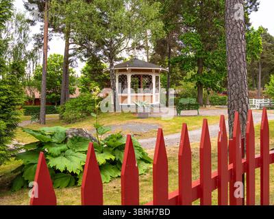 Sodertalje, Svezia - 6 giugno 2025: Un incantevole giardino con gazebo circondato da una vegetazione lussureggiante e una recinzione di picchetti rossi. Il gazebo è doloroso Foto Stock