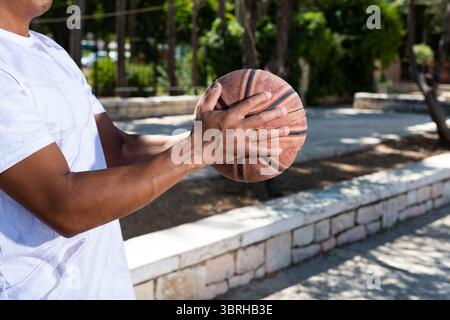Vista laterale del profilo di un giovane, atletico, afroamericano nero con braccia muscolari in una maglietta bianca che regge una pallacanestro in pelle con outstret Foto Stock